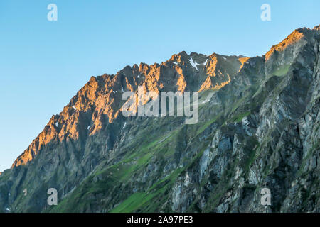 First sunbeams of the day toughing the massive, sharp stony mountain range of Schladming Alps, Austria. The mountain is partially overgrown with green Stock Photo