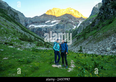 A couple standing on a meadow with the view on Schladming Alps, partially still covered with snow. Spring slowly reaching the tallest parts of the mou Stock Photo
