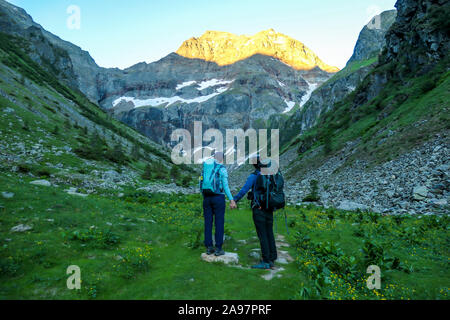 A couple standing on a meadow with the view on Schladming Alps, partially still covered with snow. Spring slowly reaching the tallest parts of the mou Stock Photo