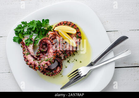 Delicious boiled octopus with lemon ,parsley and salad dressing on white plate. Traditional mediterranean seafood. Top view, flat lay Stock Photo