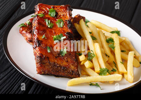 Baked short ribs in a barbecue sauce with french fries close-up on a plate on the table. horizontal Stock Photo