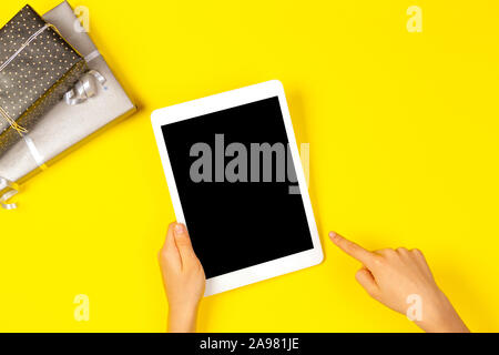 Hand finger pointing to white tablet computer and wrapped present gifts on yellow background Stock Photo