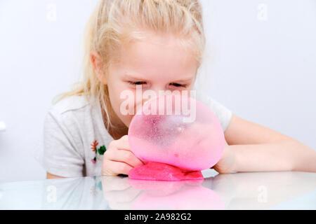 Blonde girl inflating bubble from pink glitter slime. Playing slime toy. Making slime at home Stock Photo