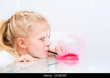 Blonde girl inflating bubble from pink glitter slime. Playing slime toy. Making slime at home Stock Photo