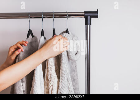 Woman choosing one of the warm cozy knitted sweaters sweaters on hangers. Stock Photo