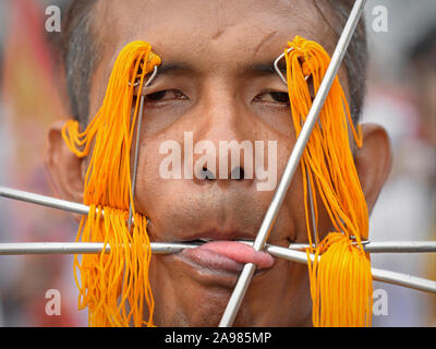 Middle-aged Thai Chinese Taoist devotee (mah song) pierces his upper eyelids, his cheeks and tongue with various long pins and decorated skewers. Stock Photo