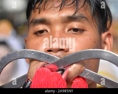 Entranced young Thai Chinese Taoist devotee pierces both cheeks with two decorated steel hooks during the Phuket Vegetarian Festival. Stock Photo