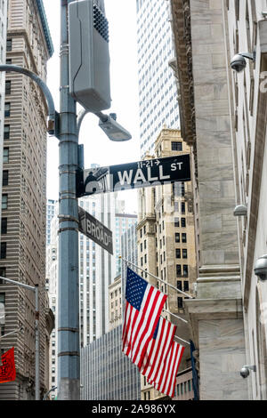 Wall St street sign with US flag flying on the New York Stock Exchange and skyscrapers in the background Stock Photo