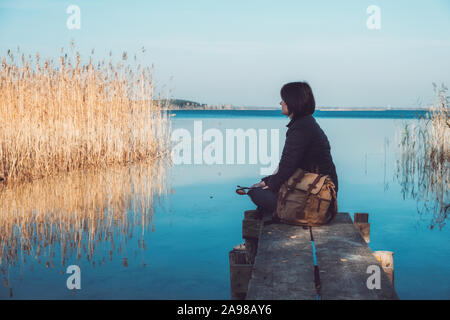 Tourist woman with backpack resting on wooden bridges on tranquil lake. Stock Photo