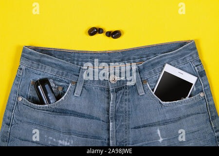 Top view of wireless headphones, jeans, charger and smartphone in its pocket on yellow background Stock Photo
