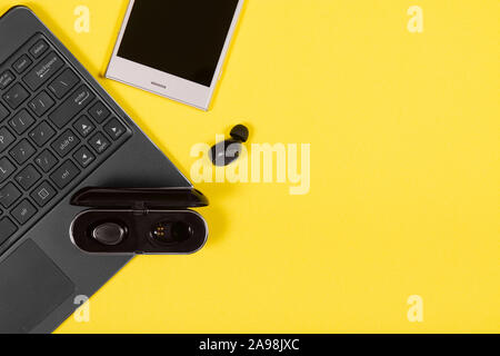 Laptop, smartphone, charging case and wireless earpieces on yellow background with copy space Stock Photo