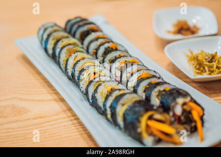 Gimbap or Kimbap is a Korean dish made from steamed white rice bap and various other ingredients, rolled in gim sheets of dried laver seaweed and Stock Photo