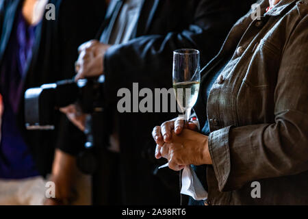 Selective focus of adult person holding a glass of alcoholic beverage in hands while standing next to a photographer  Stock Photo