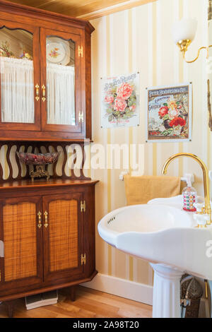 Pedestal white sink, repurposed wood with glass doors kitchen cabinets in bathroom inside an old 1920s house Stock Photo