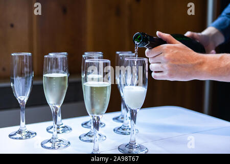 Crystal glasses that are standing on a white buffet table are being filled with an alcoholic beverage by the waiter Stock Photo