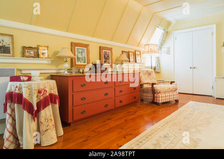Red stained wooden dresser and upholstered armchair, cream coloured rug, stained and oiled pinewood floorboards in master bedroom of old house. Stock Photo