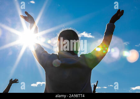 Backside and low angle view photo of person spreading arms to the sky in a participation of yoga session in nature setting Stock Photo