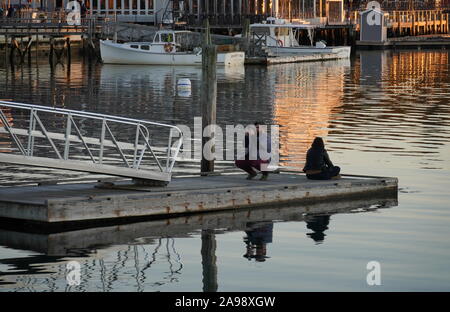 Boothbay Harbor, ME / USA - October 19, 2019: Caucasian couple take selfies on a dock during the sunset Stock Photo