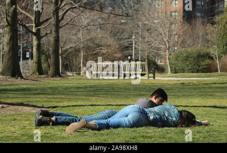 Washington, DC / USA - March 17, 2019: Mixed race couple lie down on the grass and enjoy the sun together Stock Photo