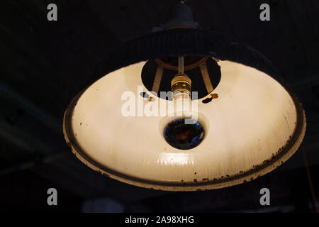 Close up view of vintage incandescent light bulb and white rusty hanging lamp. Stock Photo