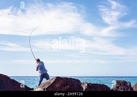 Unidentified man casting his rod from the rocks of a marina breakwater in Apollo Bay Australia Stock Photo