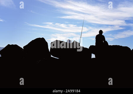 Silhouette of unidentified man fishing off breakwater rocks at Apollo Bay marina, Victoria, Australia Stock Photo