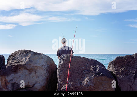 Unidentified man fishing off breakwater rocks at Apollo Bay marina, Victoria, Australia Stock Photo