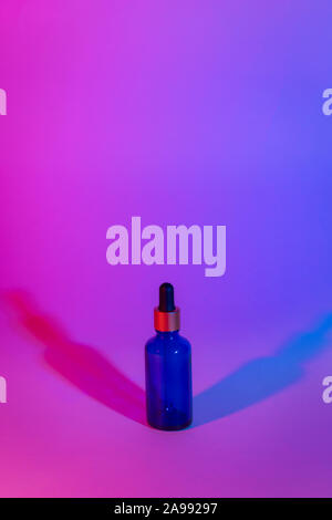 Bottle of blue transparent color on a neon trend background. Gradient from pink to blue. Two shadows of different colors. Cosmetics concept. Minimal. Stock Photo