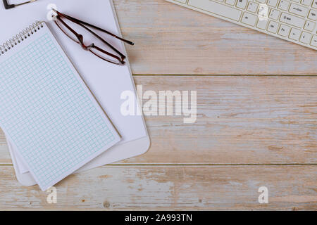 Blank open notebook with glasses and keyboard on bright wooden office desk. Stock Photo