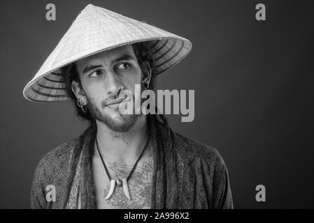 Young handsome Hispanic man with dreadlocks wearing Asian conical hat in black and white Stock Photo