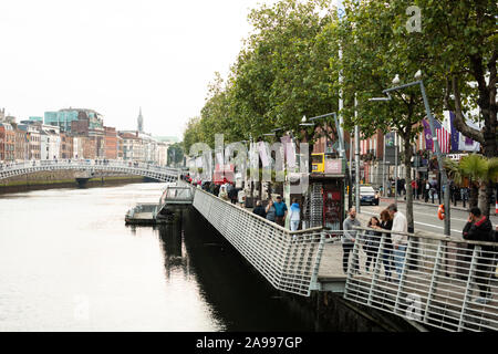 The promenade along the River Liffey and Bachelors Walk, with the dock for Dublin Discovered Boat Tours, in Dublin, Ireland, with the Ha'Penny Bridge. Stock Photo