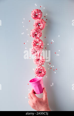 Creative image of perfect balance, tower or pyramid of tasty pink donuts balancing on bottom doughnut held by female hand. Popular hanukkah dessert. C Stock Photo