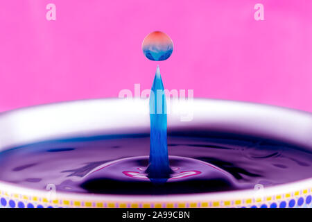 A blue and orange water drop on a pink background. Orange coloured milk dropped into blue liquid. Stock Photo