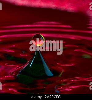 Coloured water drops released at the precise time to collide and form a shape - a drop balancing on a pyramid with a red background Stock Photo