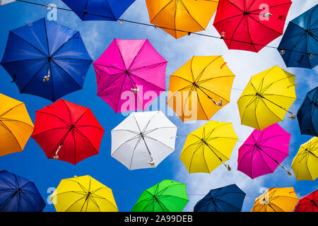 Beautiful group of colorful umbrellas hanging above the street against blue sky on a sunny day Stock Photo