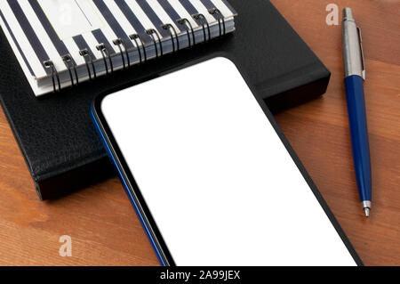 Blank screen smartphone on a wooden table next to an agenda, a notepad and a blue pen Stock Photo