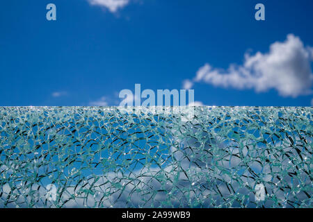 Cracked laminated glass surface against blue sky from low angle, with white clouds blurred in background Stock Photo