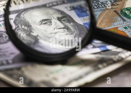 Concept on the theme of checking money for authenticity. Benjamin Franklin looks through a magnifier into the frame Stock Photo