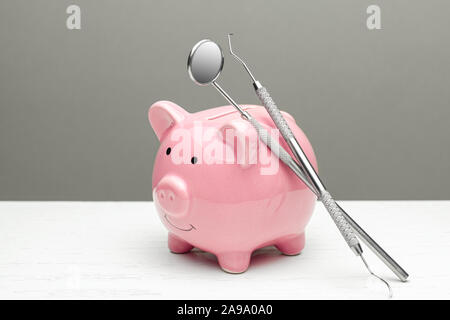 Pink piggy bank and dental tools on gray background. The concept of how to save on dental treatment. Stock Photo