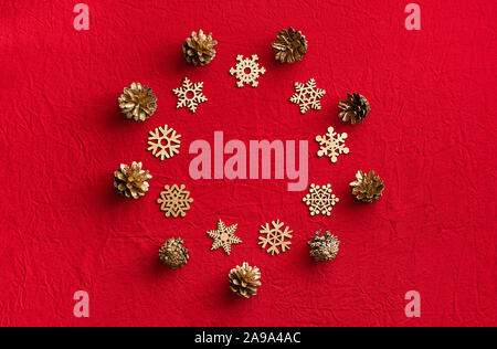 Round frame of wooden snowflakes and pine cones on a red background. Christmas zero waste concept. Flat lay, top view. Stock Photo
