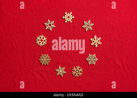 Round frame of wooden snowflakes on a red background. Christmas zero waste concept. Top view. Flat lay. Stock Photo