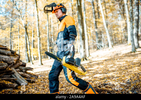 Lifestyle portrait of a professional lumberjack in protective workwear walking with a chainsaw in the forest Stock Photo