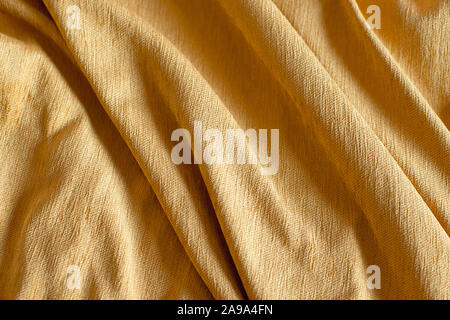 Mustard crumpled material for background or texture, tablecloth on a wooden table. Stock Photo