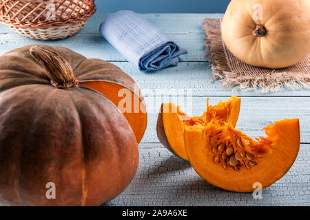 Orange and yellow pumpkins with natural imperfections and two bright orange slices on blue wooden surface. Cloth and basket at background. Selective f Stock Photo