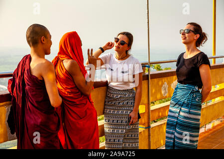 Two Female Tourists Talking To A Group Of Buddhist Monks, Su Taung Pyae Pagoda, Mandalay Hill, Mandalay, Myanmar. Stock Photo