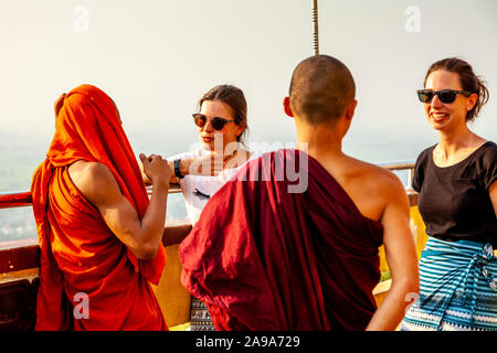 Two Female Tourists Talking To A Group Of Buddhist Monks, Su Taung Pyae Pagoda, Mandalay Hill, Mandalay, Myanmar. Stock Photo