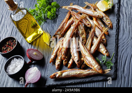 smoked smelts on a black slate tray with fresh parsley and lemon wedges, on a wooden table, view from above, close-up Stock Photo
