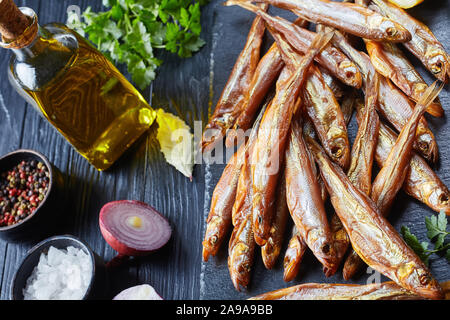 smoked smelts on a black slate tray with fresh parsley and lemon wedges, on a wooden table, view from above Stock Photo