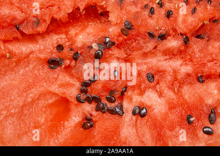 A close-up of the texture of a red fresh watermelon filling a full frame, an uneven cut with seeds and highlights, a berry was eaten with a spoon. Stock Photo