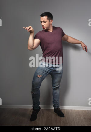 Fun humor grimacing young man showing crazy duck pose and making fun on grey background. Closeup. Full lenght Stock Photo